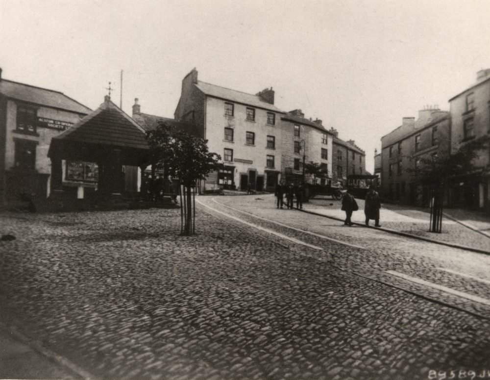 Coll. Sheila Easthope. JV series photo postcard.
Hmm, how to plac ethe date? White's shop's going, the Ewe and Lamb's sign's promnent and the Co-Op's got a sign high above its central building. The car's well dated and there's only one obvious lump of horsemuck on the cobbles.
The curley gaslamps arrived in 1913 so this is later.