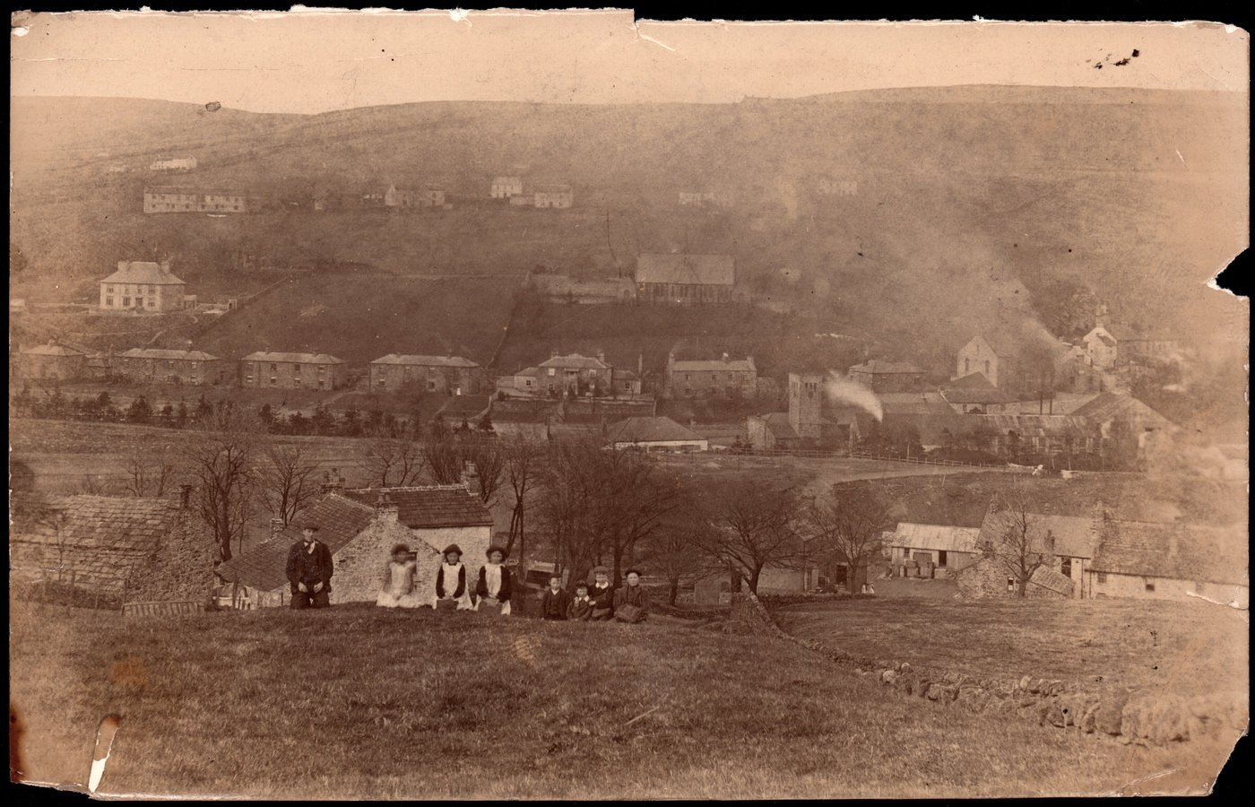 Coll. AMHS. Very fragile photographic print from the site above present-day Bevan Terrace Nenthead. A superb image of children carrying satchels- either going to or returning from school. The earlier school building was beside the public baths, market hall and Old Peter the clock on the tower. The dressing floor sits between them and the camera. Two girls wearing pinafores leave Bankfoot Stores. Image taken between 1903- building of the Vicarage, and 1906- a fire destroyed the dressing floor & the Vieille Montagne Company started to put up their new plant.